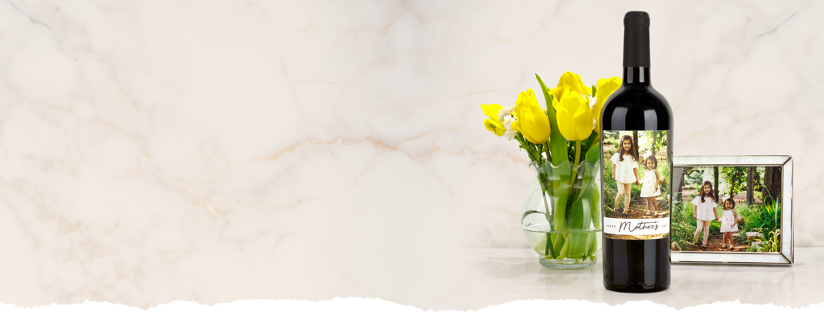 Mother's Day Wine bottle with personalized label next to a vase of yellow tulips.