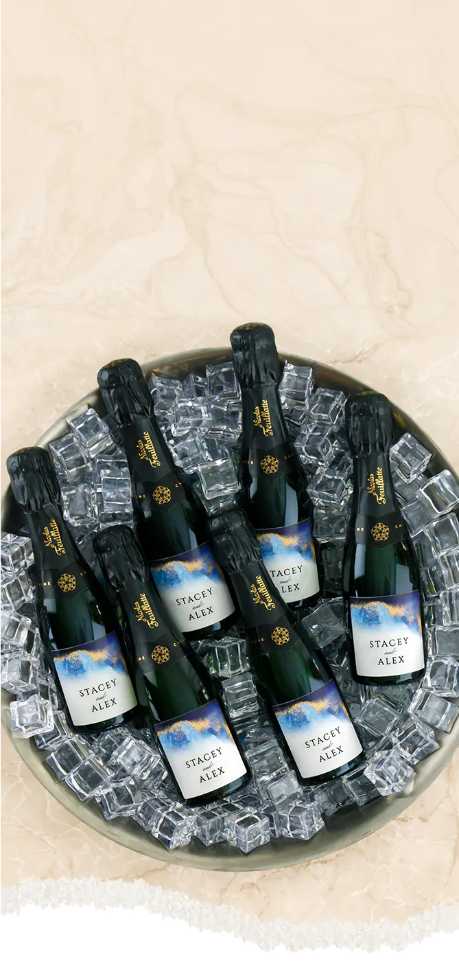 Bottles of mini Champagne bottles on ice in a decorative bowl with a beige background