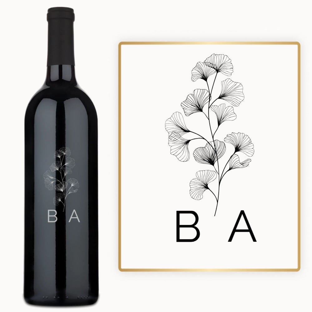Wine bottle with engraved line art flower, ginkgo leaf, and black initials B A on the label.