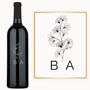 Wine bottle with engraved line art flower, ginkgo leaf, and black initials B A on the label.