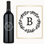 Wine bottle with a black letter B inside a floral wreath, custom engraved on the glass.