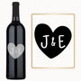 A wine bottle engraved with a heart monogram and the initials J & E, presented as an anniversary gift.