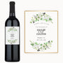 A wine bottle with a custom label showing white flowers, greenery, and the names Hailey & Colton.