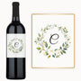 A wine bottle with a custom label featuring a floral wreath and monogram design.