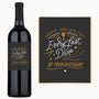A wine bottle with a custom label and card, both displaying white and gold birthday wishes.