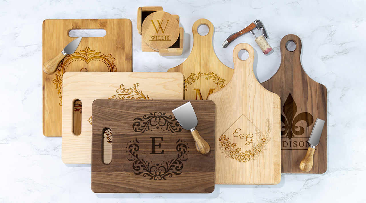 Wooden cutting boards and cheese knives with monogrammed initials displayed on a white surface.