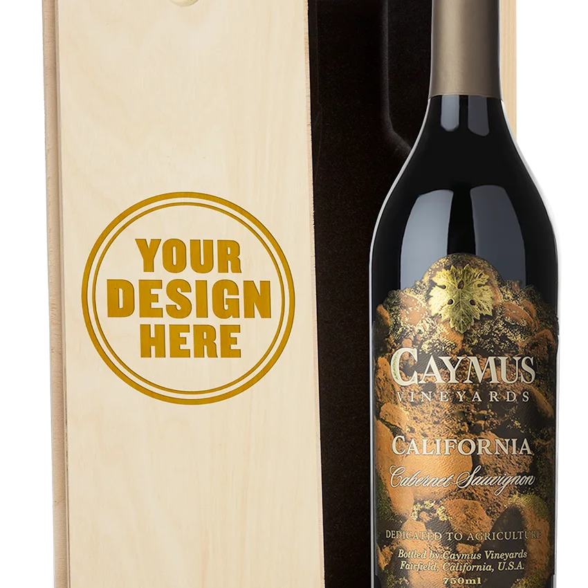 A bottle of Caymus Vineyards California Cabernet Sauvignon next to a light wood presentation box with a customizable engraving design that reads 'YOUR DESIGN HERE'.