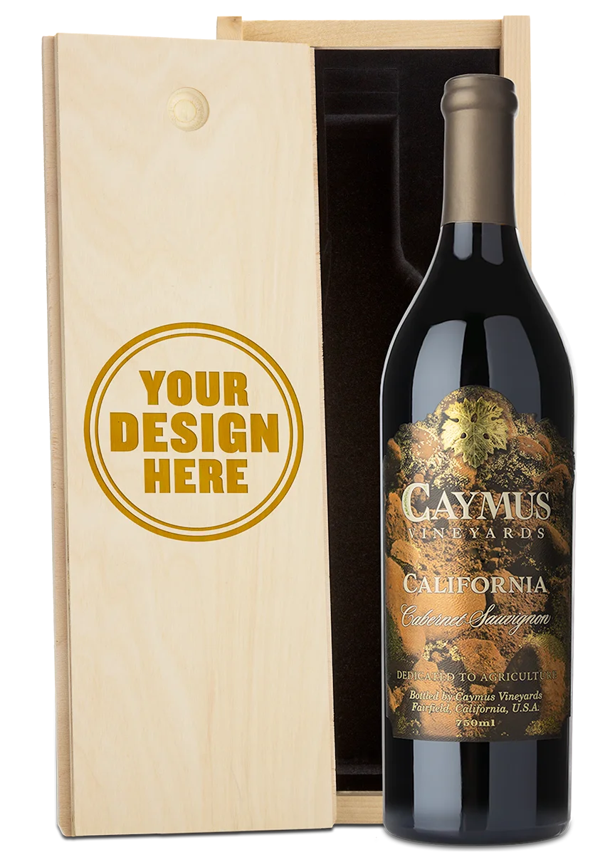 A bottle of Caymus Vineyards California Cabernet Sauvignon next to a light wood presentation box with a customizable engraving design that reads 'YOUR DESIGN HERE'.