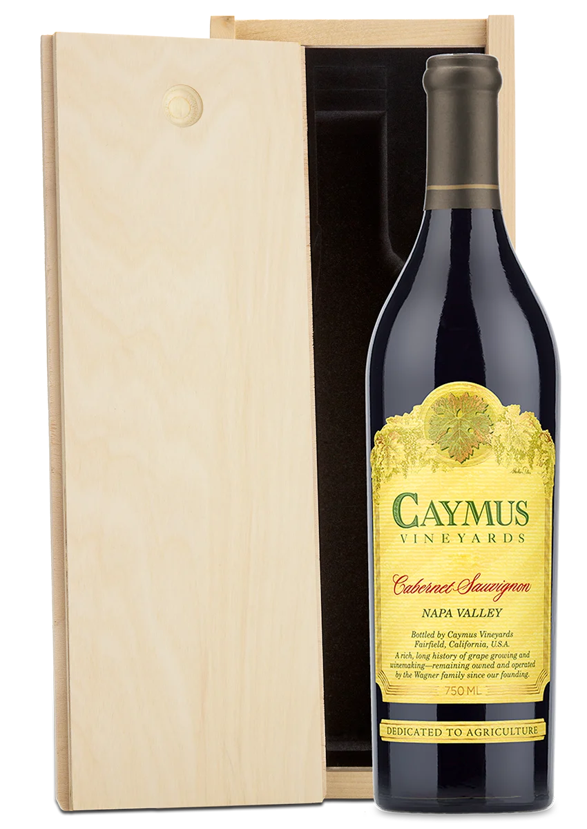 A bottle of Caymus Vineyards Cabernet Sauvignon Napa Valley next to its light natural wood presentation box on a white background.