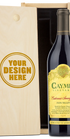 A bottle of Caymus Vineyards Cabernet Sauvignon Napa Valley red wine shown next to a light wood presentation box with a customizable design that reads 'YOUR DESIGN HERE'.