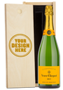 A Veuve Clicquot champagne bottle in a wood gift box with an engraved lid showing personalized text.