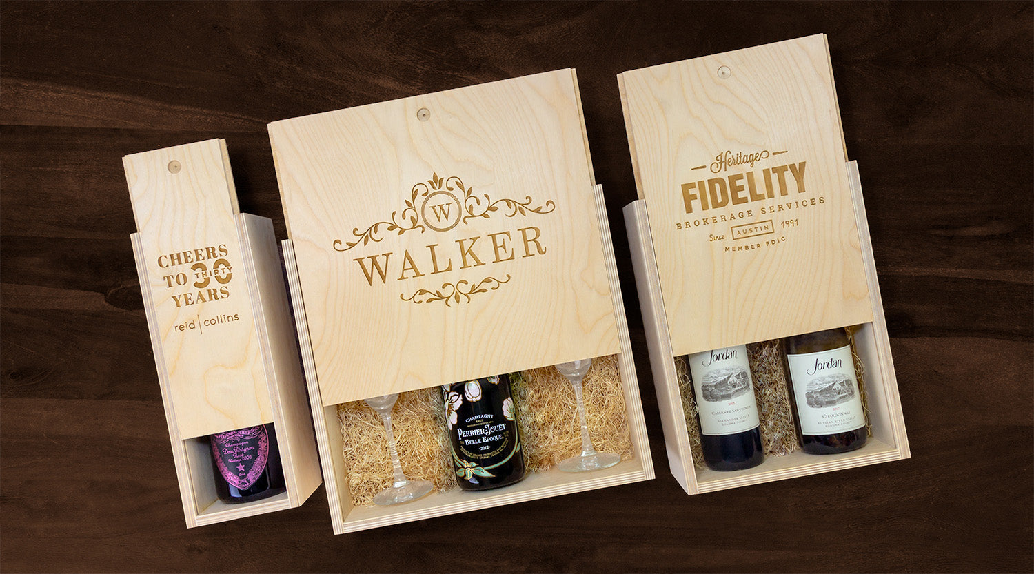 Wooden gift boxes containing wine bottles and glasses, neatly displayed on a dark wooden table.
