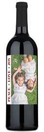 A holiday wine bottle with a festive label showing smiling girls and the words Peace Love Joy.