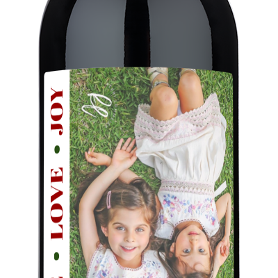 A holiday wine bottle with a festive label showing smiling girls and the words Peace Love Joy.