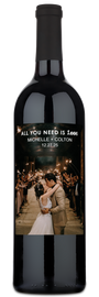 A couple kisses at their wedding surrounded by guests holding sparklers; a personalized wine bottle is in the foreground.