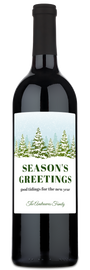 A wine bottle with a Seasons Greetings label featuring snowy trees and festive holiday decor.