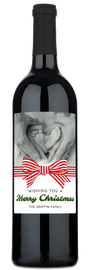Wine bottle with a label showing hands forming a heart around baby feet and topped with a festive red bow.