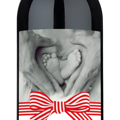 Wine bottle with a label showing hands forming a heart around baby feet and topped with a festive red bow.