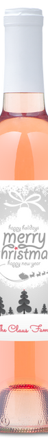 Wine bottle with label reading “Merry Christmas The Claus Family” underneath snowy trees.