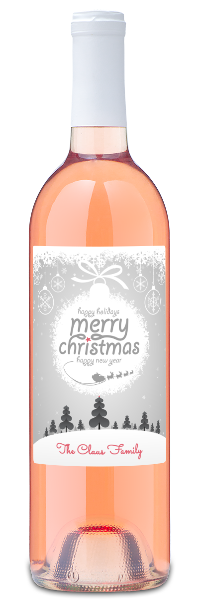 Wine bottle with label reading “Merry Christmas The Claus Family” underneath snowy trees.